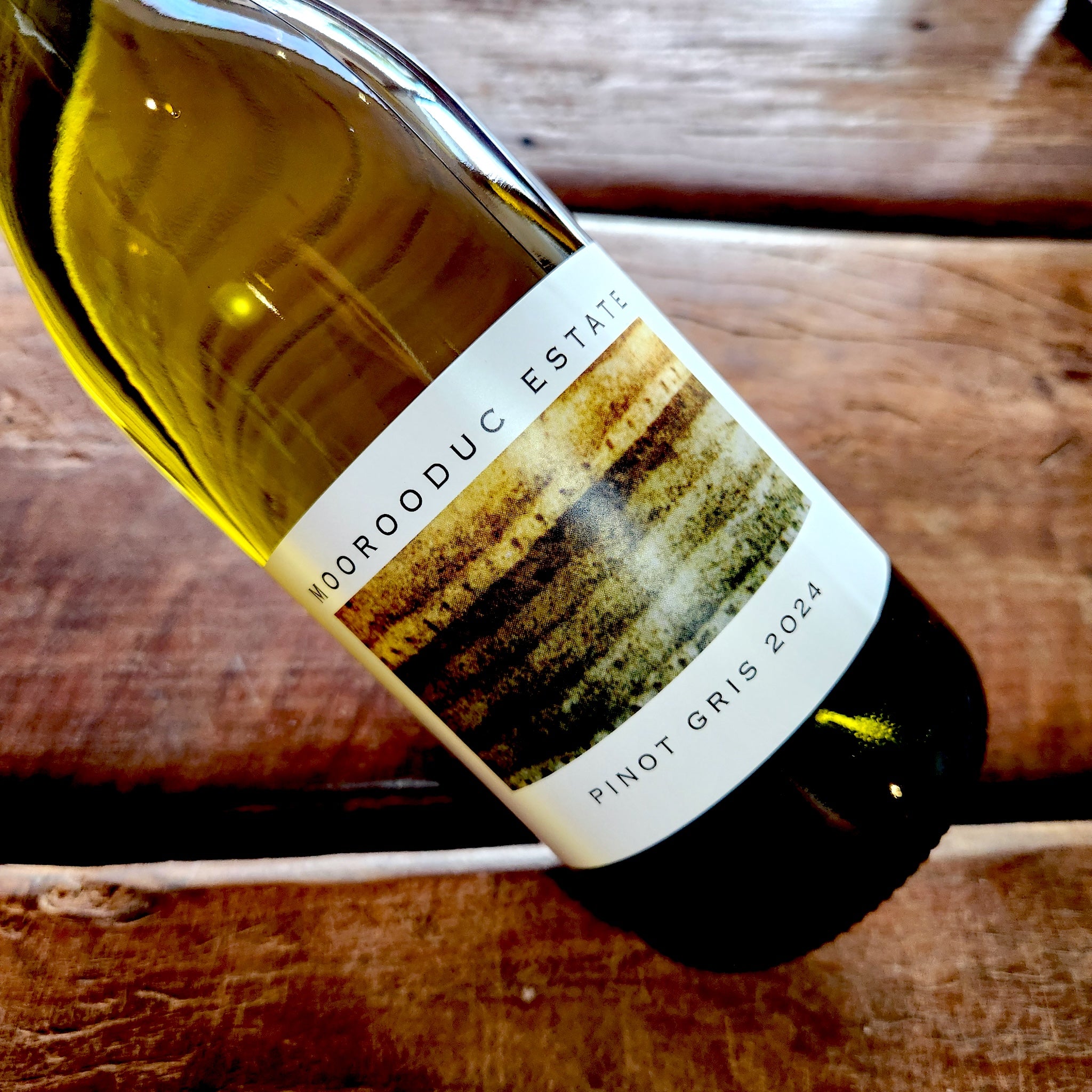 A bottle of Mooroduc Estate Pinot Gris 2024 white wine resting on a rustic wooden plank surface.