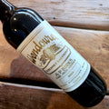 A close-up of a dark glass wine bottle lying on a rustic wooden surface, showing a white label with gold text that reads Wendouree Cabernet Sauvignon, 2024.